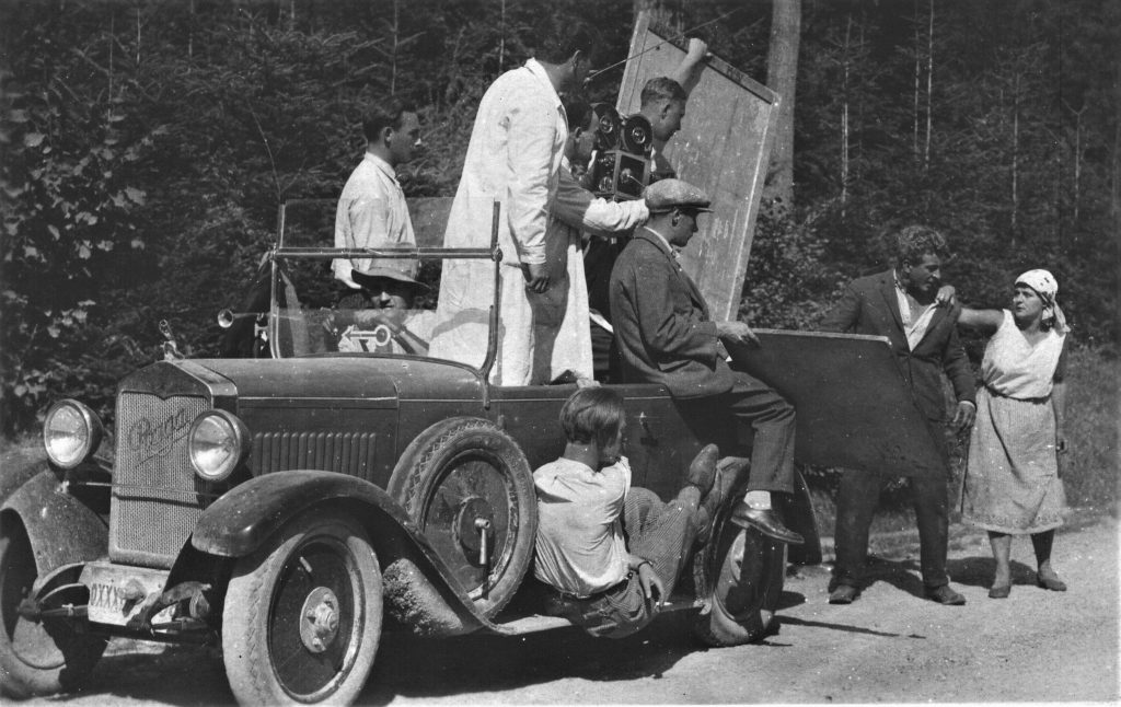 Dítě periferie, natáčení exteriérů v lesích kolem Zbraslavi. Před kamerou herec L.H.Struna a Mary Jansová. Na stupátku sedí pozdější slavný maskér Gustav Hrdlička, za kamerou v bílém plášti režisér Václav Kubásek.